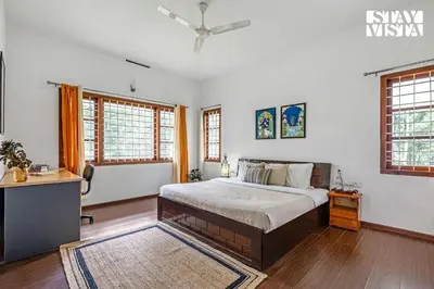 a bedroom with a bed and a desk and windows at StayVista at Wellbeing Villa in Wayanad