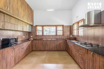 a large kitchen with wooden cabinets and a microwave at StayVista at Wellbeing Villa in Wayanad