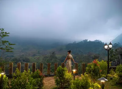 a woman standing on a fence overlooking a valley at The Grand Cliff Resort Munnar in Viripara
