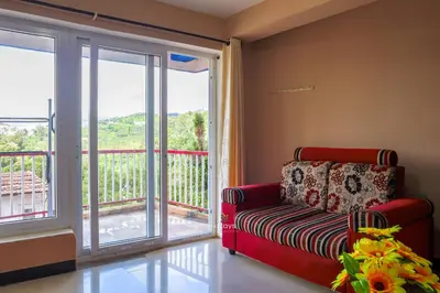 a living room with a red couch and a balcony at Vijaya Deepa Guest House by LexStays in Coonoor