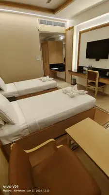 a hotel room with two beds and a television at Hotel Roopa in Mysore