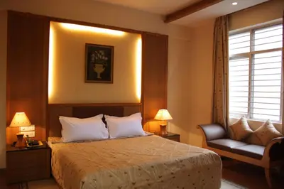 a bedroom with a bed and a chair and a window at Hotel Roopa in Mysore