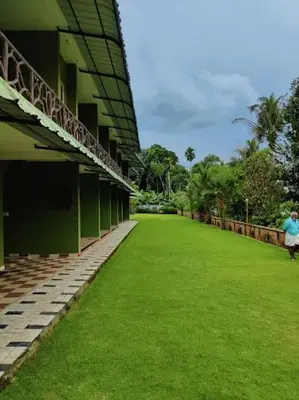 a person walking in front of a building with green grass at Elephant Pass Ayurveda & Yoga Retreat in Malayāttūr