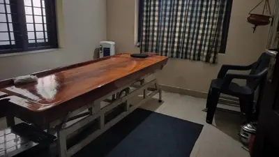 a large wooden table in a room with a chair at Aptha Ayurveda in Kadikkād