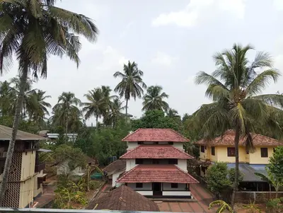 a building with a red roof and palm trees at Avalon Homes in Perintalmanna