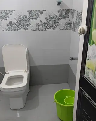a bathroom with a toilet and a green bucket at UPPU HOMESTAY in Mulappilangād