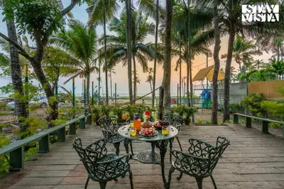 a table and chairs on a patio with palm trees at StayVista at Own The Beach Life - 1 BHK Pet Friendly - Beach View in Trichūr