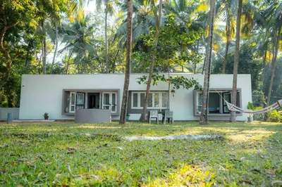 a white house with trees in front of it at Cabana by Grha - Charming Cottage at Kappad Beach in Kozhikode