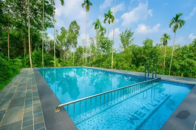 a swimming pool with palm trees in the background at Wetlands Wayanad Pool Resort with Natural Waterfalls in Padinjarathara