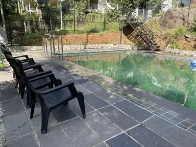 a group of chairs sitting next to a swimming pool at Wetlands Wayanad Pool Resort with Natural Waterfalls in Padinjarathara