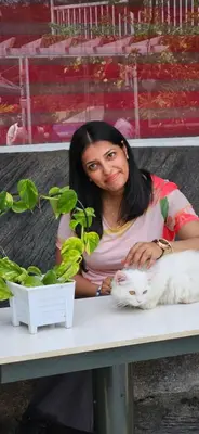 a woman sitting at a table with a white cat at S & B Dreams House in Munnar