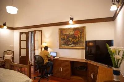 a man sitting at a desk with a computer in a room at Marlihill Bungalow - A CGH Earth SAHA Experience in Ooty