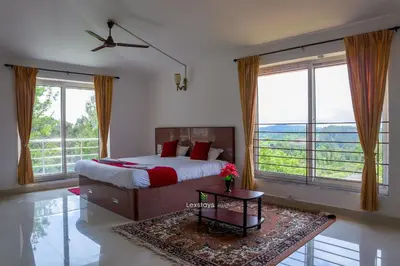 a bedroom with a bed and a table and windows at Green Premium Villa Ooty by Lexstays in Ooty