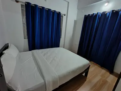 a bedroom with a bed with blue curtains and a window at Urban Nest Residence in Mysore