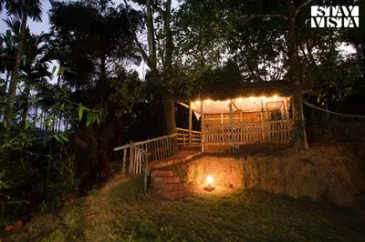 a house with a lit up porch at night at StayVista at Palm Tree Homes with Complimentary Breakfast, BBQ Grill and Pet-Friendly Home in Wayanad