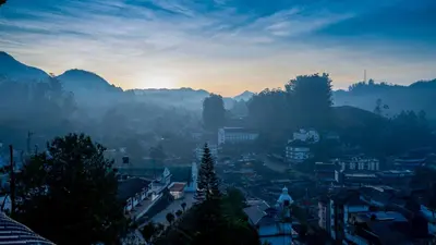 a city at sunset with mountains in the background at Carmel Top Munnar in Munnar