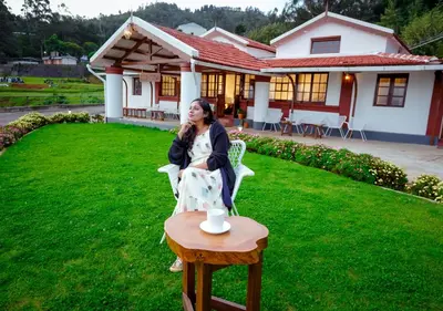 a woman sitting in a chair in front of a house at Lauriston Ooty Town Heritage Bungalow by VOYE HOMES in Ooty