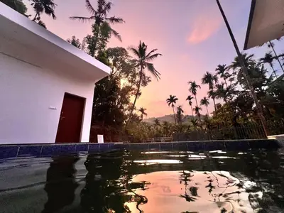 a pool in front of a house with palm trees at Nila Farms - Farm stay with a unique swimming Pool in Attappādi