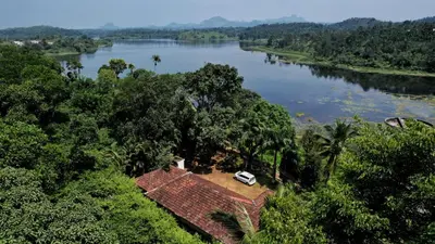 a house with a car parked on the side of a river at Winter Villa Karapuzha in Wayanad