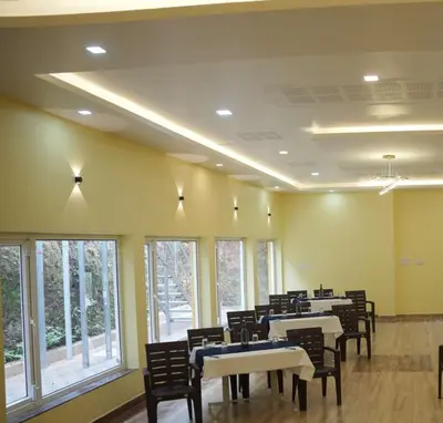 a dining room with tables and chairs and windows at Coastal Grand Resorts - Akshaya in Kotagiri