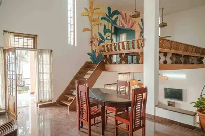 a dining room with a table and chairs and a staircase at Baywatch by Grha - A Picturesque Beachfront Villa in Kozhikode