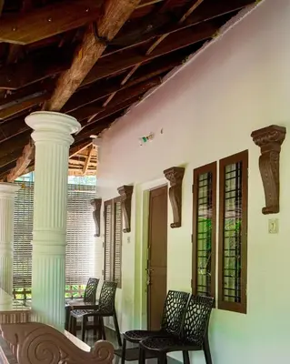 a porch with chairs and a table and a ceiling at Sanctuary View Homestay Thattekad in Ernakulam
