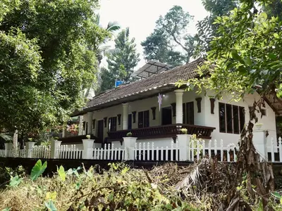 a white house with a white fence and trees at Sanctuary View Homestay Thattekad in Ernakulam