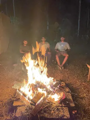 four people sitting around a fire in the woods at Senthamarai villa in Sultan Bathery