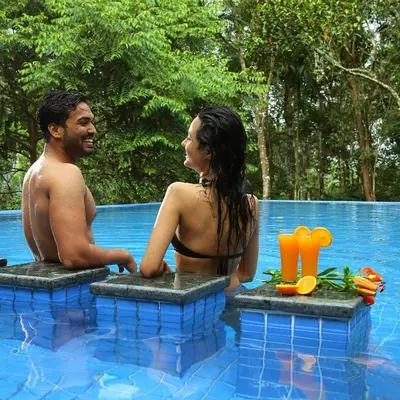 a man and a woman sitting in a swimming pool at Peter's Coffee Creek Wayanad Pool Resort in Wayanad