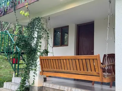 a wooden bench hanging from a house with a door at Farm stay in a coffee plantation near Athirappally in Kodali