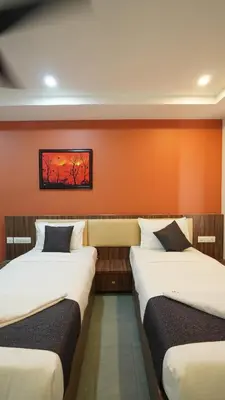 two beds in a room with an orange wall at Hotel Hive Inn - Kozhikode in Kozhikode