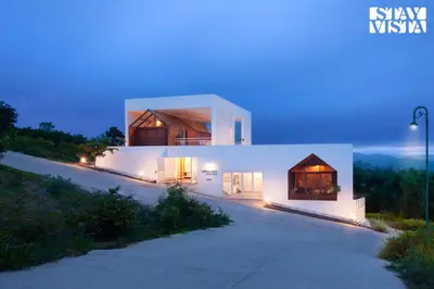 a white house with a lit up facade at night at StayVista at Reflection by The Woods - Breakfast Included - Luxury Villa in Madikeri