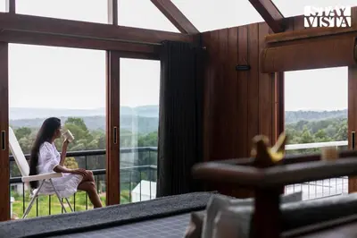 a woman sitting on a chair in a room with windows at StayVista at Reflection by The Woods - Breakfast Included - Luxury Villa in Madikeri