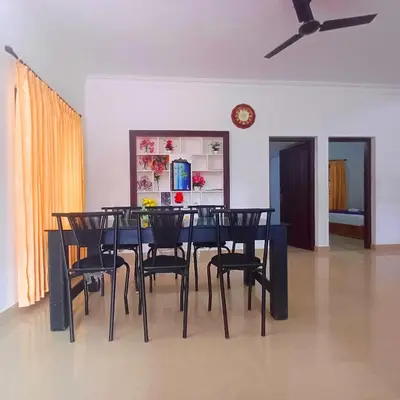 a dining room table with black chairs and a clock at Wayanad Empire Budget Villa in Kalpetta