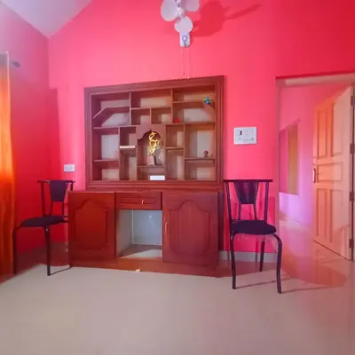 a room with a pink wall with two chairs and a cabinet at Wayanad Empire Budget Villa in Kalpetta