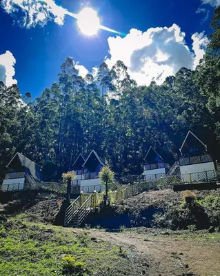 a group of houses on a hill with the sun in the sky at The Soul Of Vattavada in Vattavada