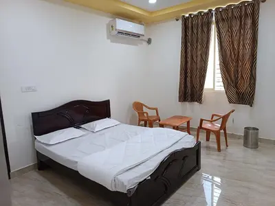 a bedroom with a bed and two chairs and a window at Govinda Krishna Comforts in Mysore