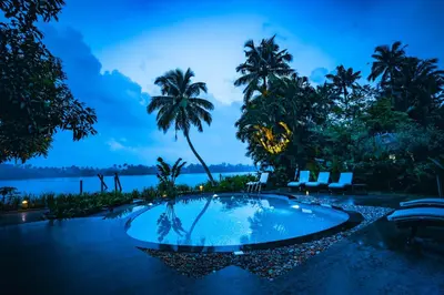 a swimming pool with a view of the water and palm trees at Vedic Village Retreat Kodungallur in Cochin