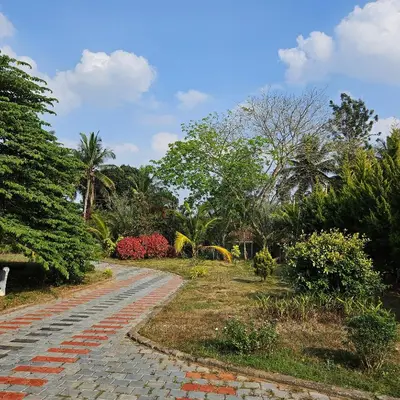 a brick path in a park with trees and bushes at Bridge Point Home Stay in Kushālnagar