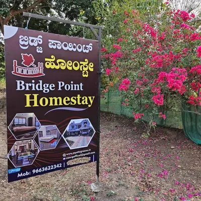 a sign for a bridge point homesteadery next to flowers at Bridge Point Home Stay in Kushālnagar