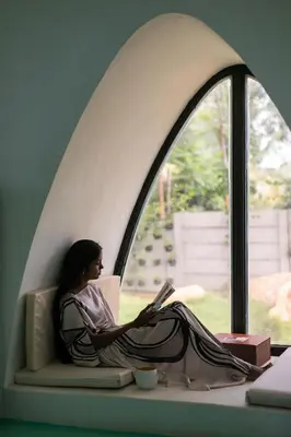 a woman sitting on a window sill using a laptop at StayVista at Shwaas 4BR Mysore with Private pool and landscape in Mysore