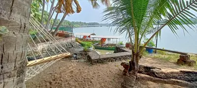 a hammock on a beach with a boat in the water at Green Island Homestay Riverside in Kozhikode