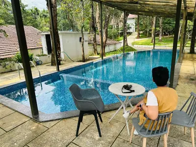 a woman sitting at a table next to a swimming pool at Drey at Druv Dakshin Farm Resort in Padinjarathara