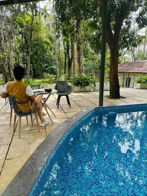 a man sitting in a chair next to a swimming pool at Drey at Druv Dakshin Farm Resort in Padinjarathara