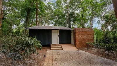 a small black and white building in a forest at Cove by Raho - Nestled Away Retreat in Siddapur