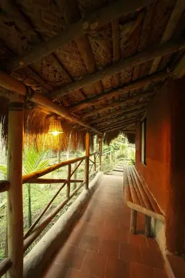 a wooden bench sitting under a building with a roof at The Soul Marayoor Mudhouse - Munnar in Marayoor