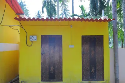 a yellow house with two doors and palm trees at Coconut Grove villa by Shivalaya Stays in Alāndurai