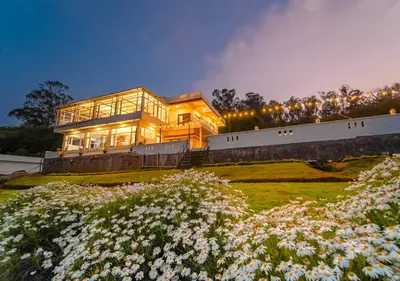 a large house on top of a hill with flowers at Silent Retreat Ooty Pool Resort by VOYE HOMES in Ooty