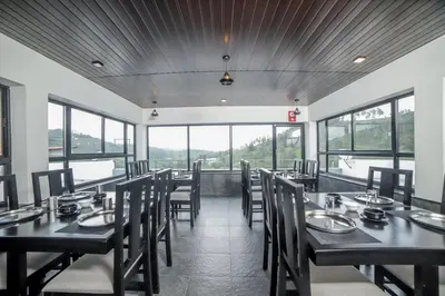 a dining room with tables and chairs and windows at Abhinav Nest by Xplore Indo in Kodanād