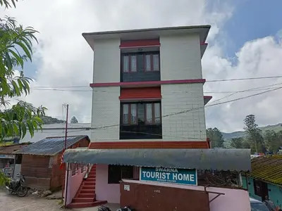 a tall house with a sign in front of it at Swarna Tourist home Munnar in Munnar